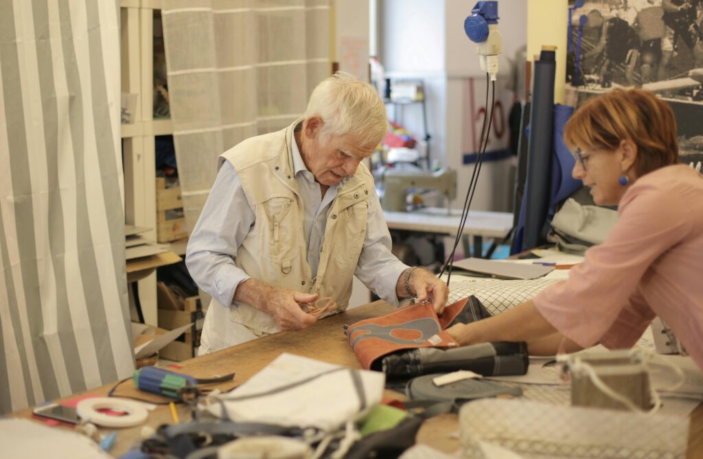 Elderly craftsman and female colleague collaborating in a workshop setting, focusing on handmade products.